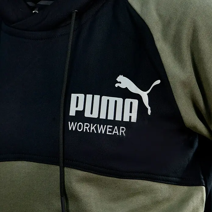 Puma Workwear Kapuzenpullover Champ - Oliv, Carbon, Größe: S - Nahaufnahme eines Puma Workwear-Hoodies in Schwarz und Olivgrün mit Logo.