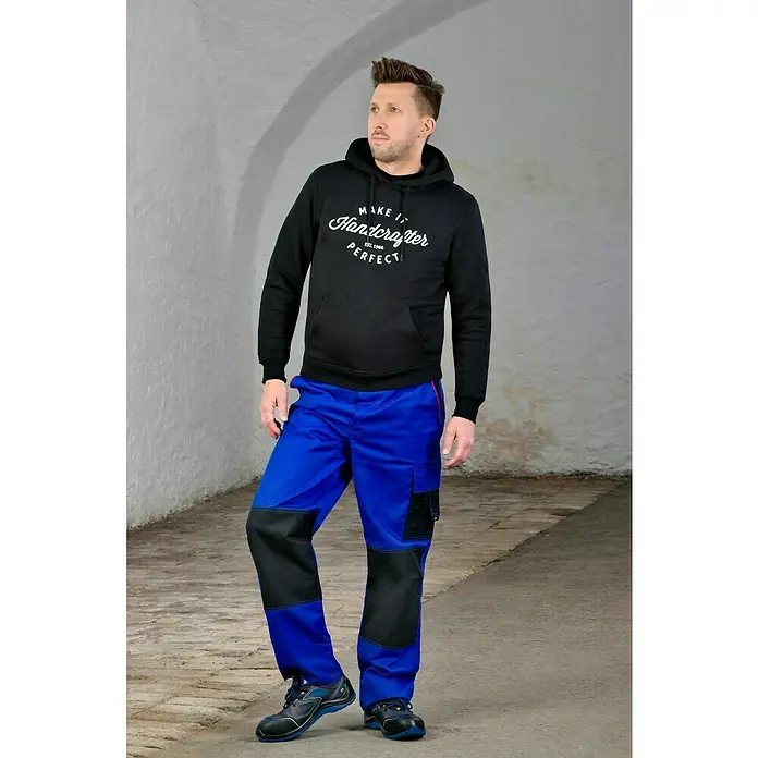 Safety Jogger Sicherheitshalbschuh Flow - 41, Schutzklasse nach EN ISO 20345: S1P, Blau, Schwarz - Ein Mann, der eine schwarze Kapuzenjacke und blaue Arbeitshosen trägt. Bequeme und strapazierfähige Kleidung für den Arbeitsalltag.
