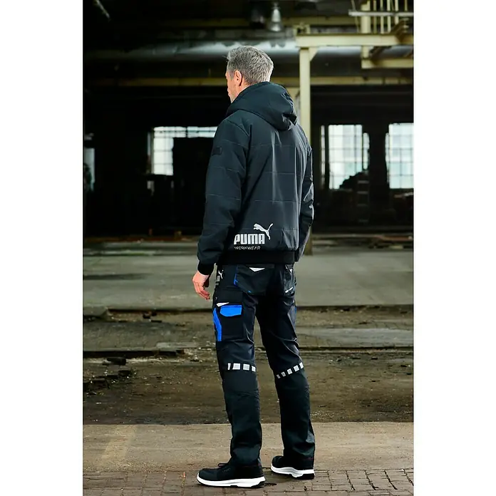 Puma Workwear Winterjacke Champ - Carbon, L - Rückenansicht eines Mannes in Puma-Arbeitskleidung, bestehend aus Jacke mit Kapuze und Arbeitshose.