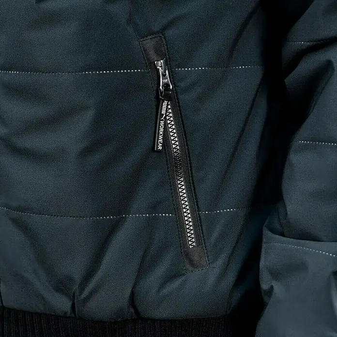 Puma Workwear Winterjacke Champ - Carbon, L - Detailansicht einer schwarzen Puma Workwear Jacke mit Reißverschluss und Logo-Anhänger, die robuste und funktionale Arbeitskleidung betont.