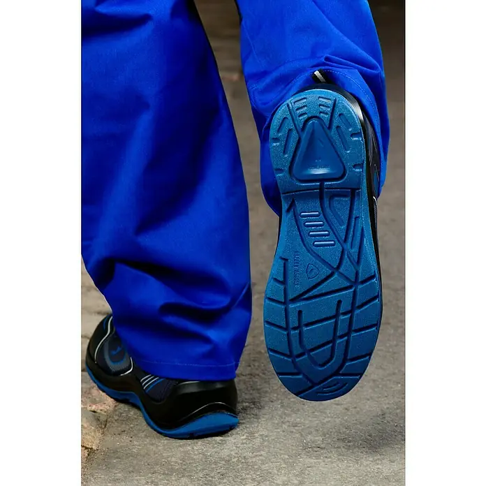 Safety Jogger Sicherheitshalbschuh Flow - 41, Schutzklasse nach EN ISO 20345: S1P, Blau, Schwarz - Detailaufnahme eines blauen Schuhs mit schwarzem Obermaterial und blauer Sohle, getragen mit einer blauen Arbeitshose.
