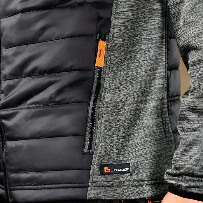 L.Brador Hybridjacke 6090P - Schwarz/Grau, L - Detailaufnahme einer schwarzen Steppjacke mit grauem Ärmel und orangefarbenem Reißverschlussdetail, Label „Labrador“ sichtbar.