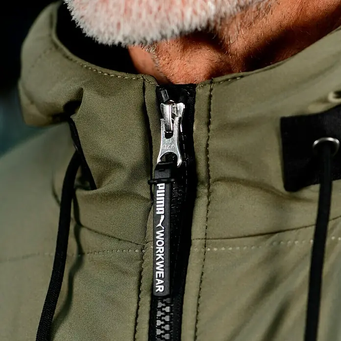 Puma Workwear Winterjacke Champ - Oliv/Carbon, S - Nahaufnahme einer olivgrünen Puma Workwear Jacke mit Reißverschluss und Kapuze, ideal für Arbeitskleidung.