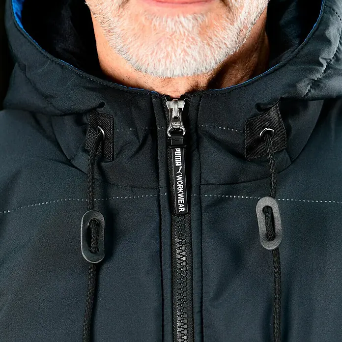 Puma Workwear Winterjacke Champ - Carbon, L - Nahaufnahme einer schwarzen Puma-Arbeitsjacke mit Reißverschluss und Kapuze, ideal für den Einsatz im Freien.