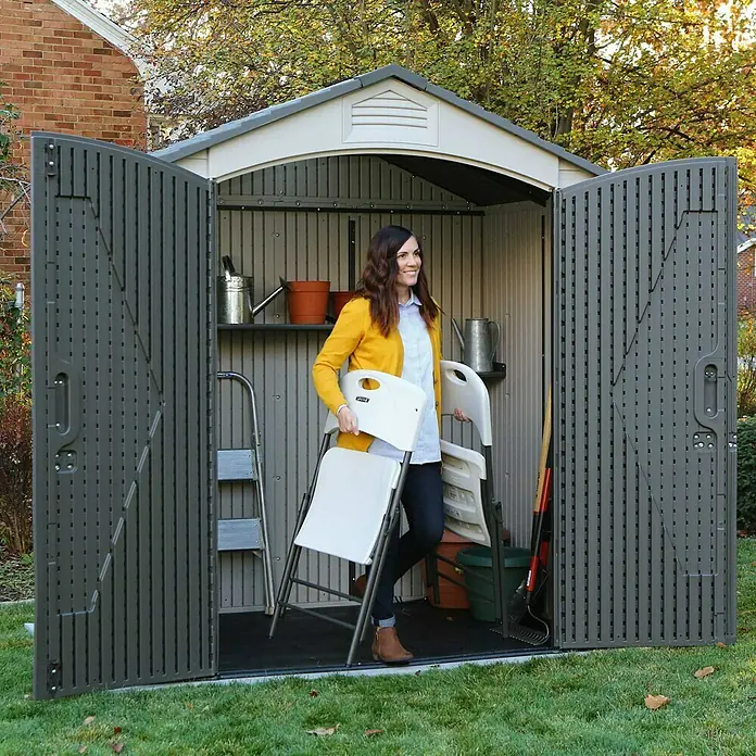 Lifetime Gerätehaus Starlet - 215 cm, 140 cm, Kunststoff, Anthrazit/Grau - Eine Frau verlässt ein LifeTime Gartenhaus mit Klappstühlen. Das Haus ist gefüllt mit Gartengeräten und hat ein graues Dach.