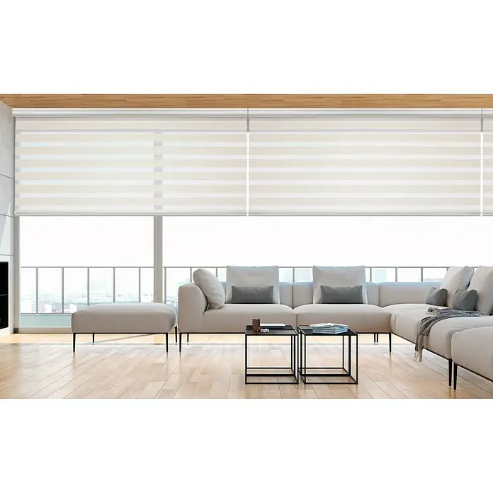 Estor noche y día Platinum - An x Al: 200 x 250 cm, Lino - Una vista moderna de la sala de estar con persianas enrollables beige que brindan privacidad mientras filtran la luz, complementada con un elegante sofá.