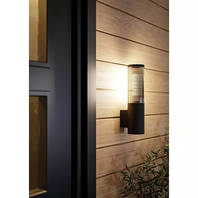 Eglo Aplique exterior Salle - 15 W, 7,5 x 31 cm, Negro, IP54 - Aplique de pared exterior negro con difusor de cristal estriado, proyectando luz cálida sobre una pared de madera.