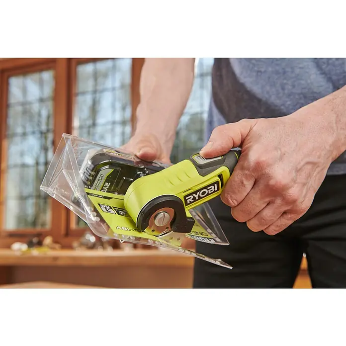 Ryobi 4V USB Akku-Universalschere RCT4-120G - 4 V, 1 Akku, 2 Ah - Eine Nahaufnahme eines RYOBI ONE+ Akku-Rotationsschneiders in der Verpackung, gehalten von einer Person. Das Werkzeug ist grün und schwarz.