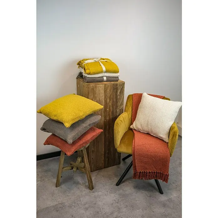 Decke Kent - Golden Yellow, 170 x 130 cm, 100 % Baumwolle - Einrichtungsidee mit gestapelten Kissen in Gelb, Grau und Rostrot, Decken und einem senfgelben Sessel mit cremefarbenem Kissen und rostfarbener Decke.