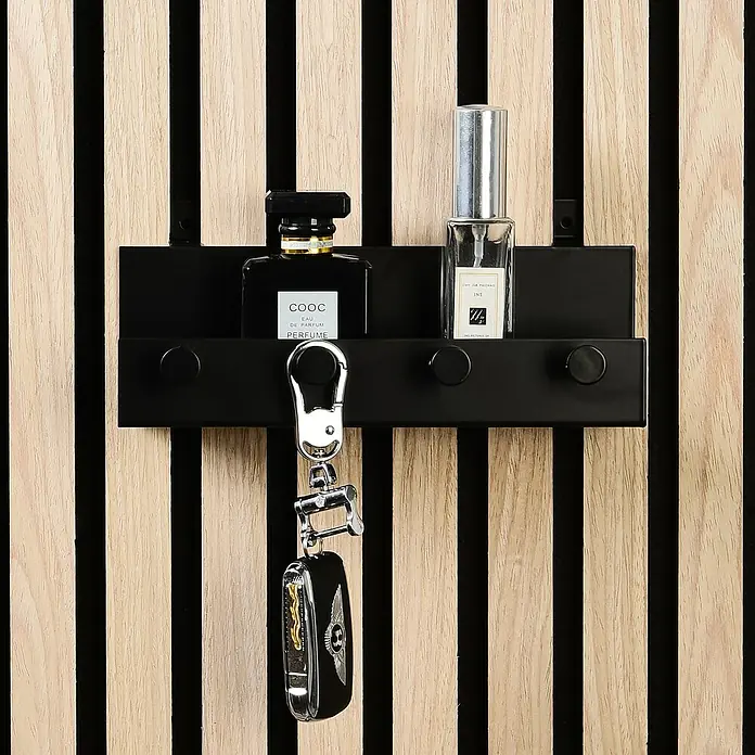 Millex Regal - L x B x H: 5 x 21,5 x 7 cm, Passend für: Akustikpaneele, Montageart: Einhängen - Ein schwarzes Schlüsselbrett mit zwei Parfümflaschen und einem Autoschlüssel, das an einer Wand mit Holzpaneelen hängt.