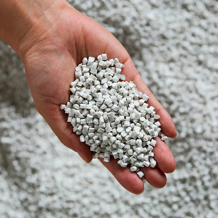 Ecopots Amsterdam Pflanzkübel rund - Außenmaß (Ø x H): 30 x 25,9 cm, Kunststoff, Braungrau, Mit Bewässerungssystem - Eine Handvoll weiße Kunststoffgranulate, die als Rohstoff für verschiedene Produkte dienen, vor einem verschwommenen Hintergrund.