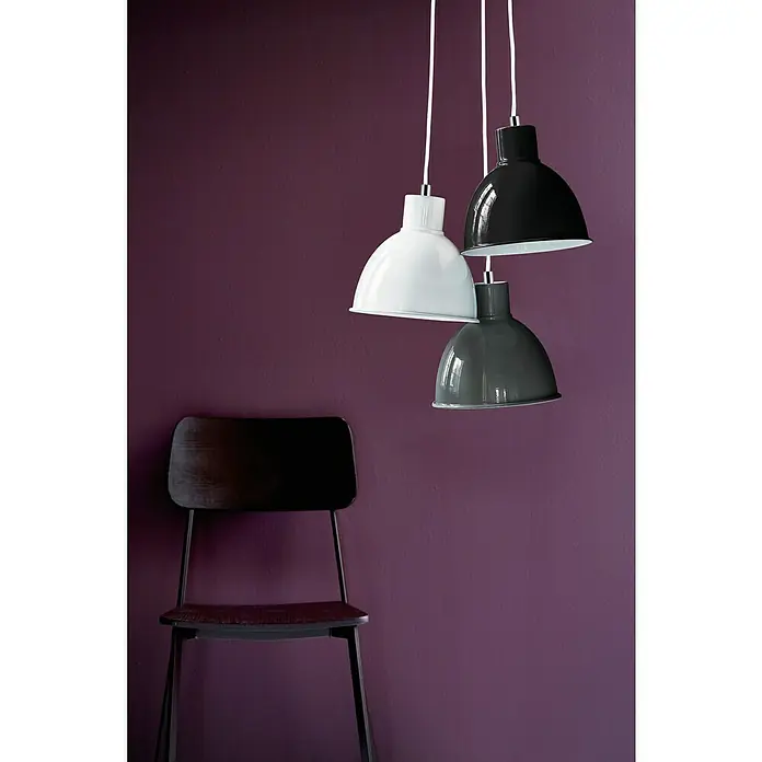 Nordlux Lámpara colgante redonda Pop - 60 W, Ø x Al: 21,5 x 23 cm, Negro, E27 - Tres lámparas colgantes de colores (blanco, gris, negro) cuelgan frente a una pared púrpura. Una silla de madera oscura a la izquierda.