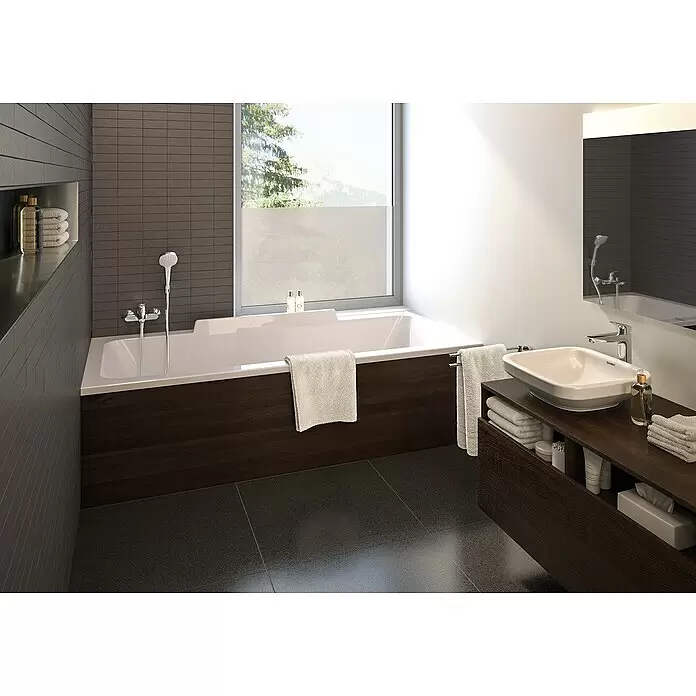 Hansgrohe Logis Grifo monomando de bañera - Profundidad del grifo: 194 mm, Cromo, Brillante - Baño moderno con bañera rectangular blanca y panel de madera oscura, complementado con un lavabo rectangular blanco sobre un mueble de madera oscura a juego.