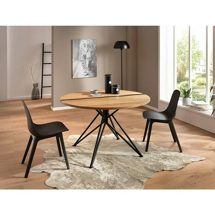 Exclusivholz Tischplatte Epoxid - Eiche, Durchmesser: 120 cm, Stärke: 2,6 cm - Das Bild zeigt einen Esstisch mit Holzplatte und schwarzem Metallgestell, umgeben von zwei schwarzen Stühlen auf einem Fellteppich.