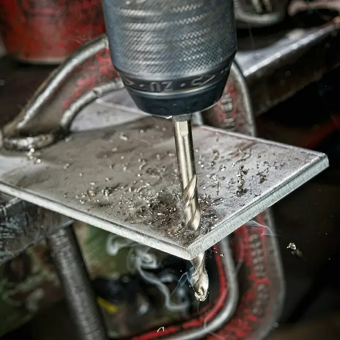 DeWalt Broca para metal DT4914-QZ - 1 ud., Diámetro de la broca: 10 mm - Broca metálica perforando un agujero en una pieza de metal sujeta con una abrazadera. Sale humo.