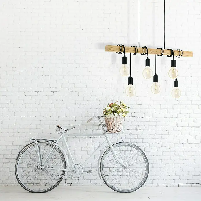 Eglo Townshend Pendelleuchte - B x H: 10 x 110 cm, Schwarz/Braun, 360 W - Eine rustikale Holzbalken-Pendelleuchte mit schwarzen Akzenten und Edison-Glühbirnen hängt über einem weißen Fahrrad mit Blumenkorb.