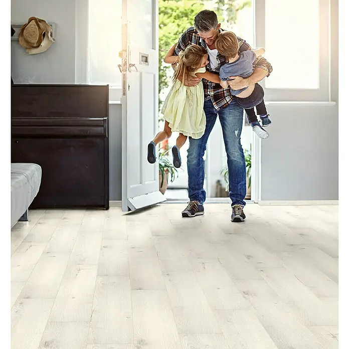 Krono Original Laminat Organic Flex - Pearl River Oak, Landhausdiele, 1.288 x 189 x 7 mm - Heller Laminatboden im Wohnbereich mit einem Mann, der seine Kinder umarmt und in die Luft hebt, für eine freundliche Atmosphäre.