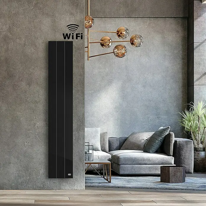 HJM Emisor térmico Vertical Ixora - 1.000 W, Negro, 10 x 25,5 x 150 cm, Cerámico - Elegante panel de calefacción negro con función WiFi montado en una pared gris, complementado con una lámpara moderna y un sofá gris al fondo.