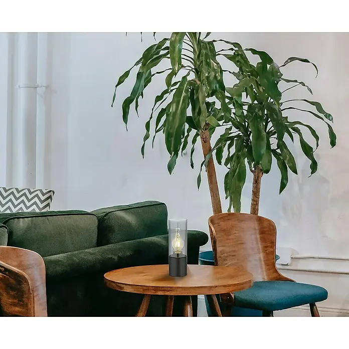 Globo Lámpara de sobremesa Annika - 25 W, Ø x Al: 9 x 30 cm, Negro, E27 - Elegante lámpara de mesa con bombilla Edison sobre una mesa de madera, rodeada de muebles verdes y una planta en maceta.