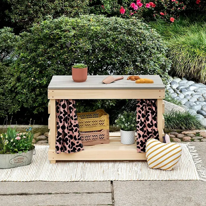 Muddy Buddy Kindertisch zum Matschen Little Leo - L x B x H: 80 x 40 x 55 cm, Holz, Natur/ Puderrosa - Ein hölzerner Spieltisch mit Vorhängen, Pflanzen und Spielzeug im Garten, ideal für kreatives Spielen im Freien.