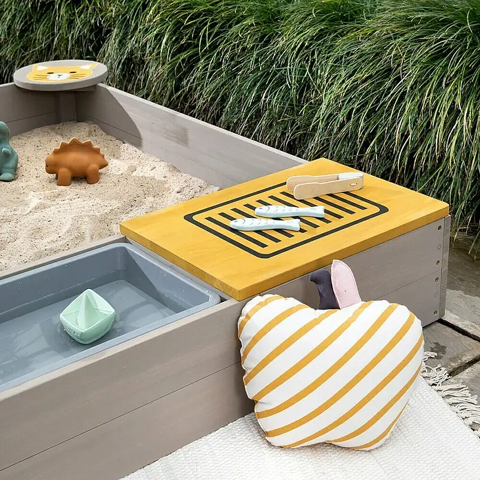 Muddy Buddy Sandkasten Wild Cat - 120 x 120 x 20 cm, Holz, Warmgrau/ Ocker - Ein Sandkasten mit Spielzeug und einer Apfelkissen. Ideal für kreatives Spielen im Freien.
