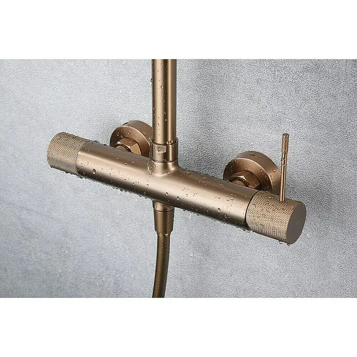 Imex Line Sistema de ducha - Con grifo monomando, Oro rosa - Primer plano de un moderno grifo de ducha de bronce con gotas de agua sobre una pared gris.