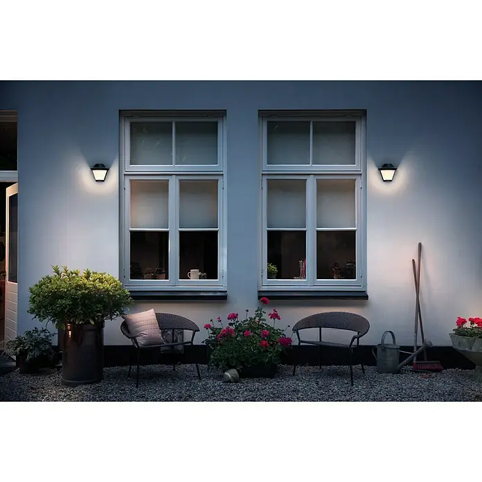 Philips Aplique exterior Serres - 60 W, 133 x 182 x 170 mm, Negro, IP44 - Encantadora escena exterior con dos elegantes luces de pared que iluminan la casa, creando un ambiente acogedor en el jardín.