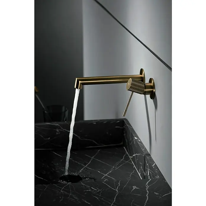 Imex Line Grifo de lavabo empotrado - Oro - Primer plano de un moderno grifo dorado de pared sobre un lavabo de mármol negro.