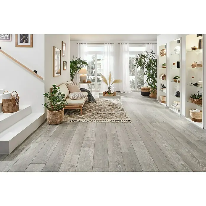 LOGOCLIC Vinto Laminat Classic Eiche Rossano1.288 x 195 x 8 mm, Landhausdiele, Eiche Rossano - Helle Holzböden verleihen diesem gemütlichen Wohnzimmer mit Sofa, Teppich und Pflanzen ein modernes und einladendes Ambiente.