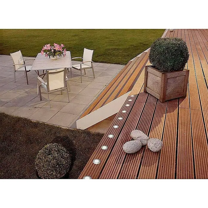 Lutec Foco de jardín LED Hony Deck - 1 W, Plateado, IP67, LED - Un espacio al aire libre con una tarima de madera con luces empotradas, junto a una jardinera con un arbusto redondo.