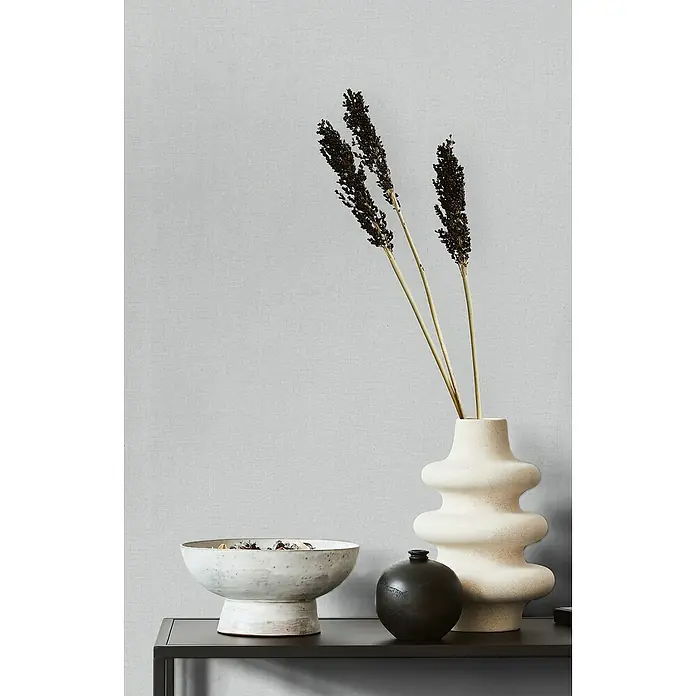 Marburg Struktura Vliestapete Kylie - Grau, Uni, 10,05 x 0,53 m - Stillleben mit einer beigen Vase mit Trockenblumen, einer Schale mit Potpourri und einer kleinen schwarzen Vase auf einem schwarzen Tisch.