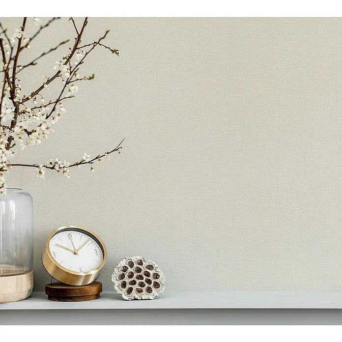 Marburg Struktura Vliestapete Jackie - Hellbeige, Uni, 10,05 x 0,53 m - Nahaufnahme eines Tisches mit einer Blumenvase, einer goldenen Uhr und einer Samenkapsel. Dekorative Elemente schaffen eine ruhige Atmosphäre.