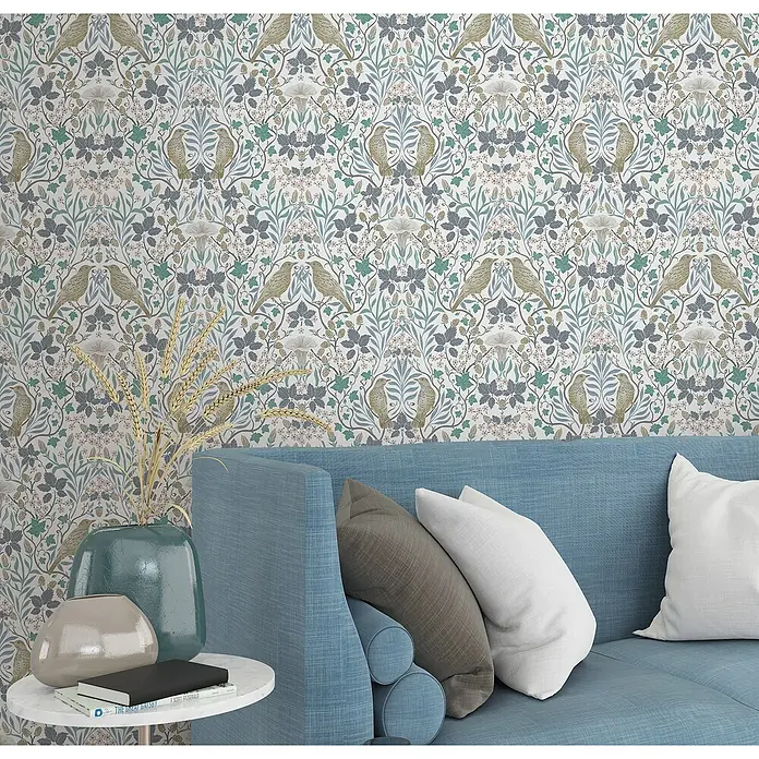 Marburg Heritage Vliestapete Tiere & Blumen - Weiß/Grün/Blau, Floral, 10,05 x 0,53 m - Wanddekoration mit floralem Muster und Vogelmotiven über einem blauen Sofa mit Kissen, schafft eine gemütliche Atmosphäre.