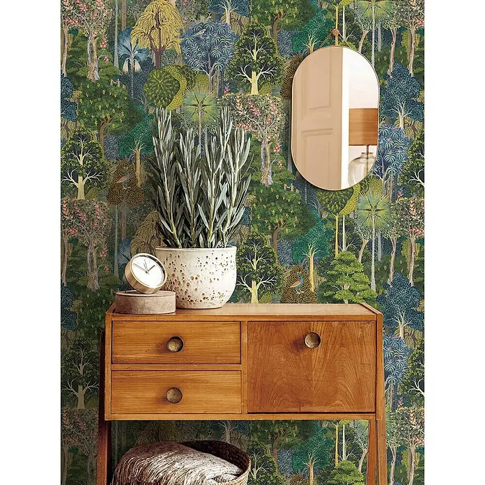 Marburg Heritage Vliestapete Gemaltes Waldmotiv - Grün/Blau, Floral, 10,05 x 0,53 m - Dekorative Kommode aus Holz mit Uhr, Pflanze und Spiegel vor einer Tapete mit Waldmotiv.