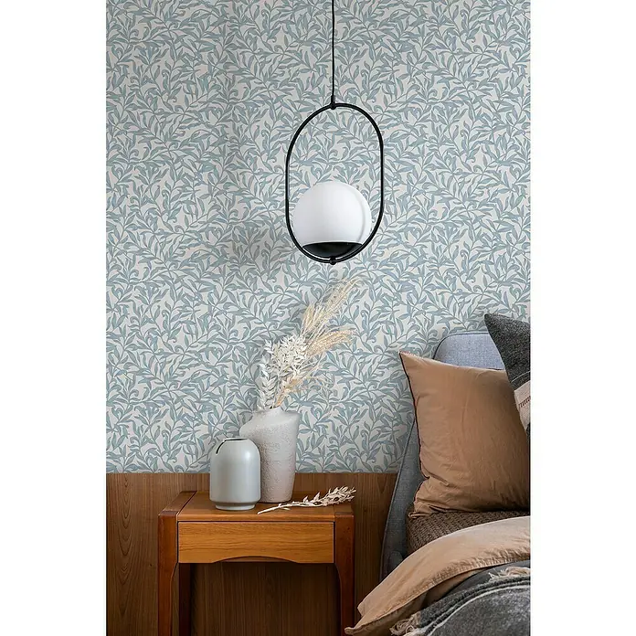 Marburg Heritage Vliestapete Blätterranken-Allover - Blau/Grau, Floral, 10,05 x 0,53 m - Zimmerdekor mit floral gemusterter Tapete, einem Nachttisch aus Holz mit Vasen und einer modernen Hängelampe mit kugelförmigem Schirm.