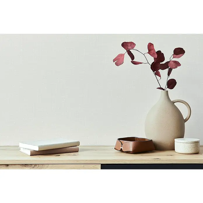 Marburg Heritage Vliestapete Vintage-Look - Beige, Uni, 10,05 x 0,53 m - Nahaufnahme eines dekorierten Tisches mit Büchern, einer Lederschale, einer Vase mit Blättern und einer kleinen Dose.