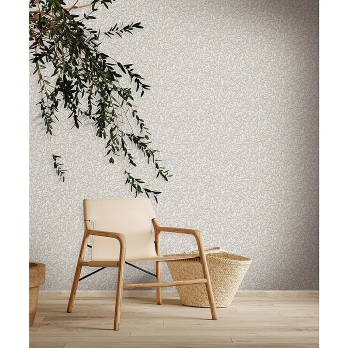 Marburg Heritage Vliestapete Blätterranken-Allover - Beige/Grau, Floral, 10,05 x 0,53 m - Stilvoller Sessel mit Holzrahmen und hellem Lederbezug neben einem geflochtenen Korb vor einer Wand mit Blättermuster.