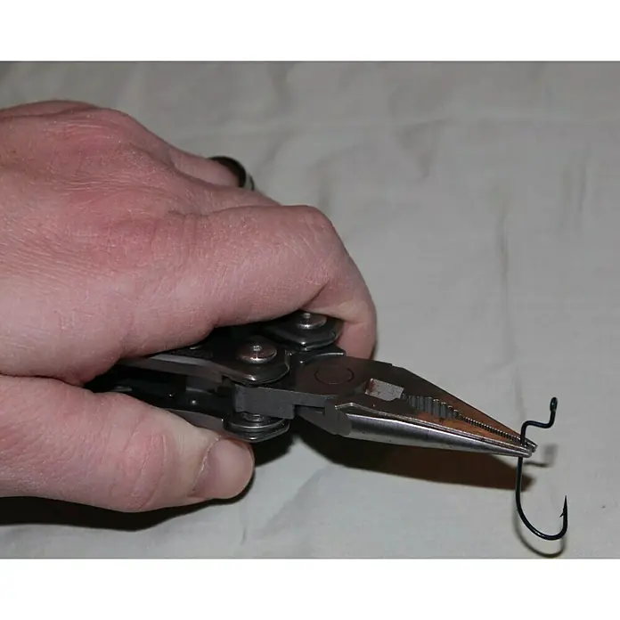 Gerber Alicates multiuso plegable Suspension - Acero inoxidable - Una mano sujeta unos alicates que sujetan un anzuelo de pesca. La herramienta es versátil y útil para pescadores y actividades al aire libre.