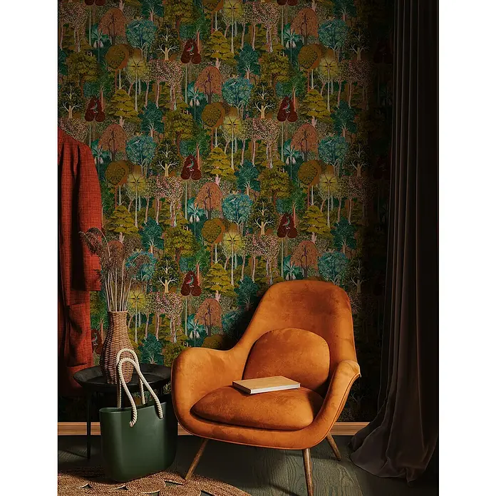 Marburg Heritage Vliestapete Gemaltes Waldmotiv - Grün/Braun, Floral, 10,05 x 0,53 m - Gemütliche Leseecke mit orangefarbenem Sessel, Bücher und grüner Tragetasche vor einer kunstvollen Waldtapete.