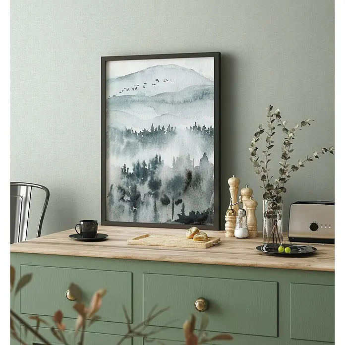 Marburg Heritage Vliestapete Glatte Struktur - Blau, Uni, 10,05 x 0,53 m - Ein gerahmtes Aquarellbild mit einer Waldlandschaft in Grau- und Blautönen. Das Bild hängt an einer Wand über einem grünen Sideboard.