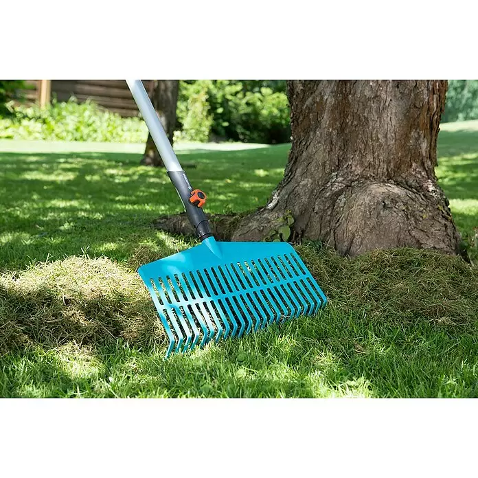 Gardena Combisystem Kleingeräte-Set - 4 -tlg. - Blauer Gardena Rechen, der an einen Haufen geharkten Grases neben einem Baum im Garten lehnt.