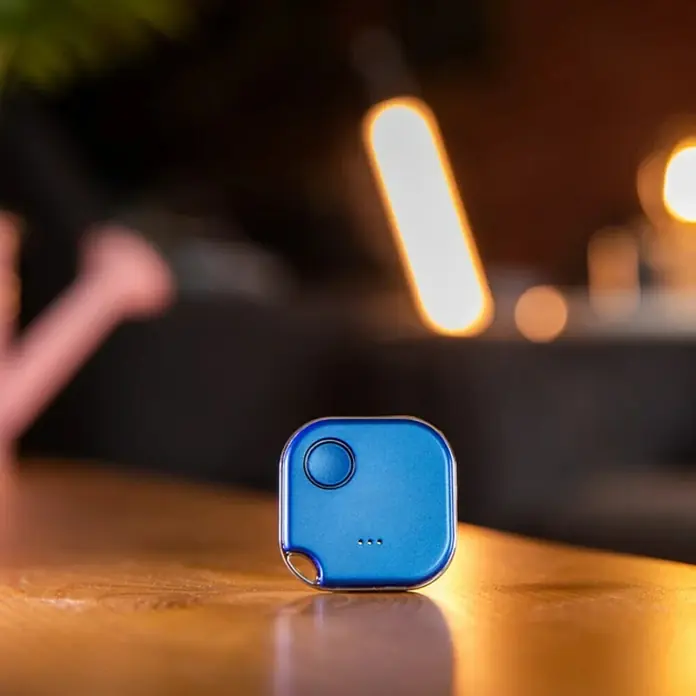 Shelly Schalter BLU Button1 - Blau, Batteriebetrieben - Nahaufnahme eines blauen quadratischen Smart Trackers auf einem Holztisch, der sich ideal zum Auffinden von Schlüsseln oder Gepäck eignet.