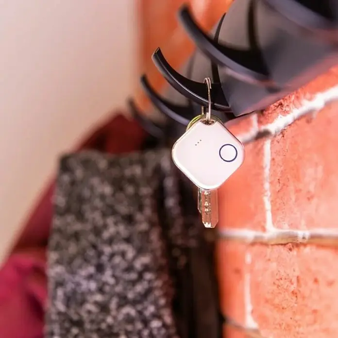 Shelly Schalter BLU Button1 - Weiß, Batteriebetrieben - Schlüsselanhänger mit Tracker hängt an einem Haken an einer Ziegelwand.