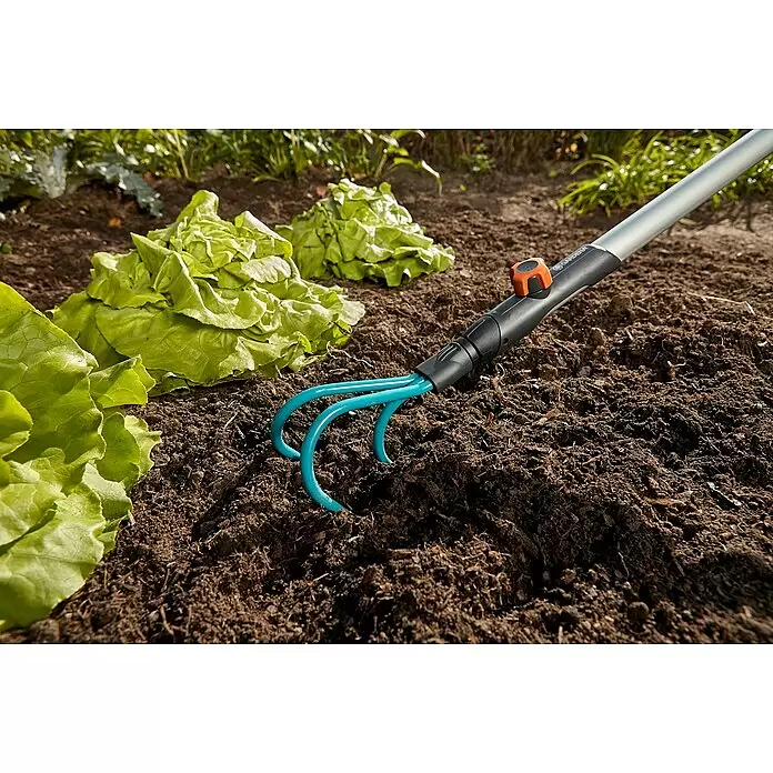 Gardena Combisystem Kleingeräte-Set - 4 -tlg. - Blaue Grubberzinken in Gartenerde neben grünem Salat, mit schwarzem Griff und orangefarbenem Drehknopf.