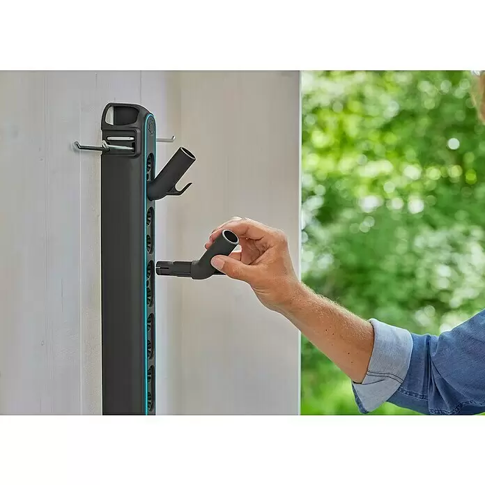 Gardena Combisystem Kleingeräte-Set - 4 -tlg. - Eine Person befestigt einen dunkelgrauen modularen Haken an einem schwarzen, wandmontierten Aufbewahrungssystem mit blauen Akzenten.