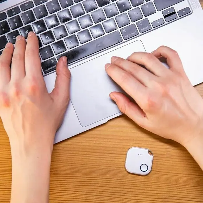 Shelly Schalter BLU Button1 - Weiß, Batteriebetrieben - Draufsicht auf einen Laptop in Verwendung mit einem weißen Tile Tracker auf einem Holztisch, der zum Auffinden von Gegenständen dient.