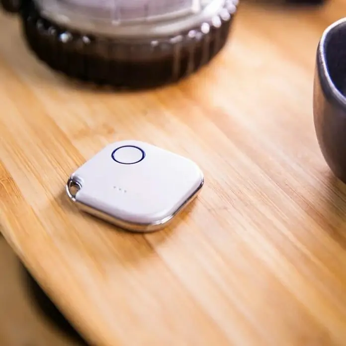 Shelly Schalter BLU Button1 - Weiß, Batteriebetrieben - Ein weißer, quadratischer Bluetooth-Tracker mit silbernem Rand liegt auf einem Holztisch. Ideal zum Auffinden von Gegenständen!