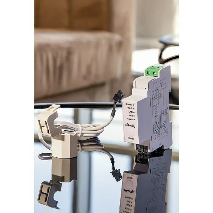 Shelly Wechselstromzähler Pro EM - 50 - 50 A, 110 V - 240 V - Das Bild zeigt einen Shelly 3EM Energiezähler mit einem Stromsensor, der auf einer spiegelnden Oberfläche steht.
