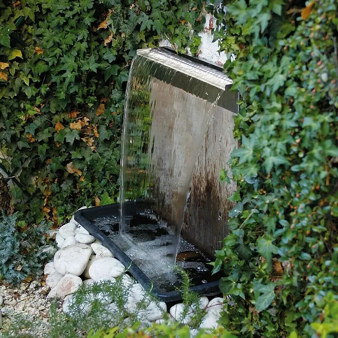 Ubbink Einbau-Wasserfall Niagara LED 60 Set - 12,5 x 60 x 10 cm, Edelstahl, Leuchtmittel: LED - Nahaufnahme eines modernen Wasserfalls im Garten mit Kaskade und Becken, umgeben von üppigem Grün.
