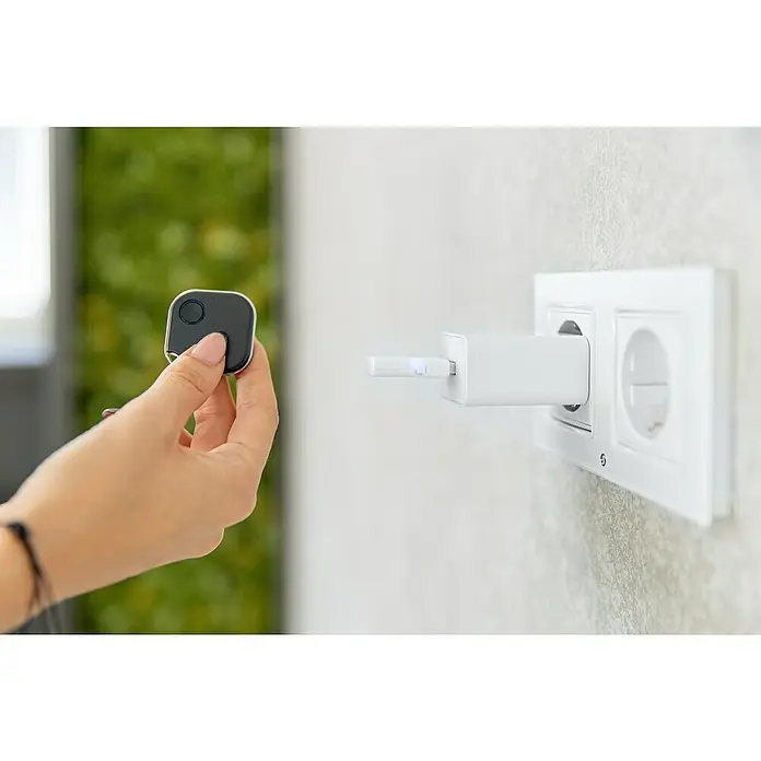 Shelly Gateway BLU - 2.400 MHz - 2.483,5 MHz - Aufladen eines schwarzen Smart-Trackers mit einer weißen Ladestation in einer Wandsteckdose.